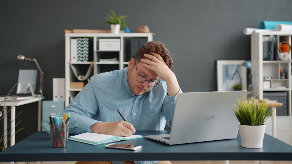 A man at his desk looking stressed while writing